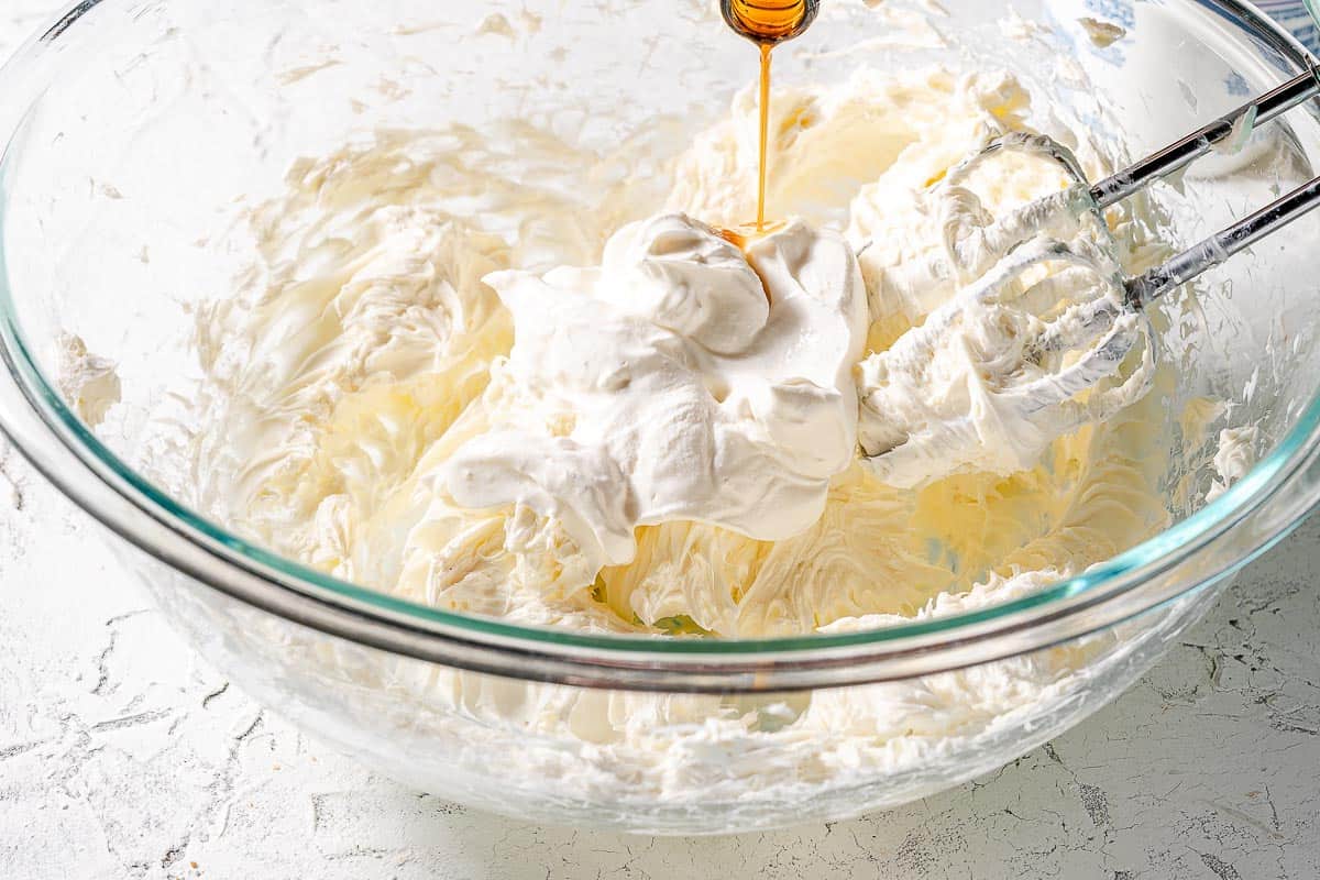 vanilla being poured into bowl with cream cheese and sour cream