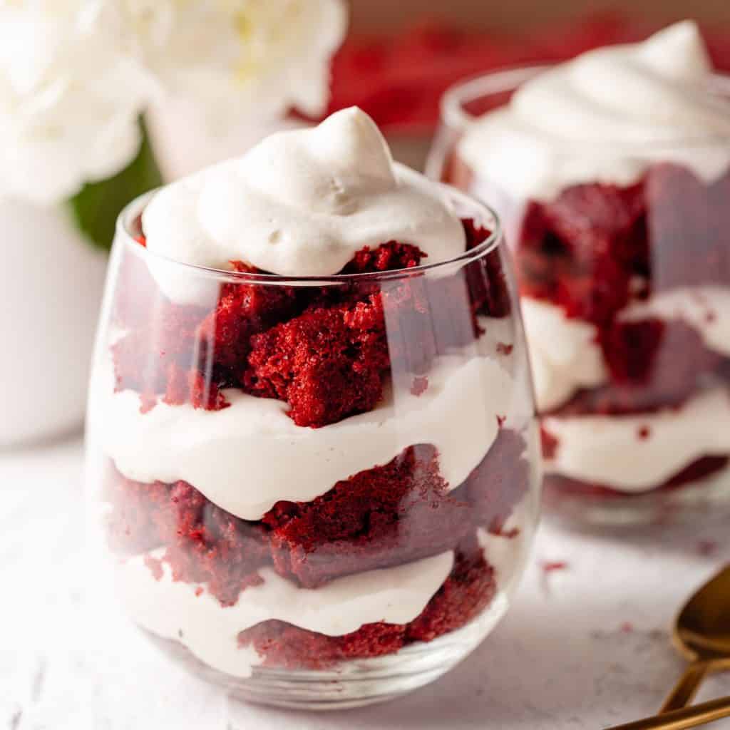 red velvet cheesecake trifles in 2 wine glasses with flowers in the background