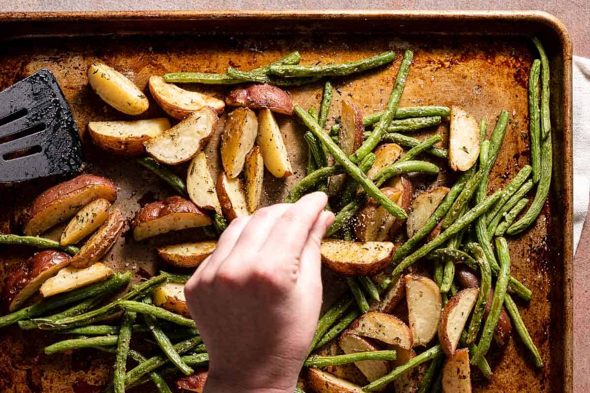 hand sprinkling pepper on top of cooked potatoes and green beans
