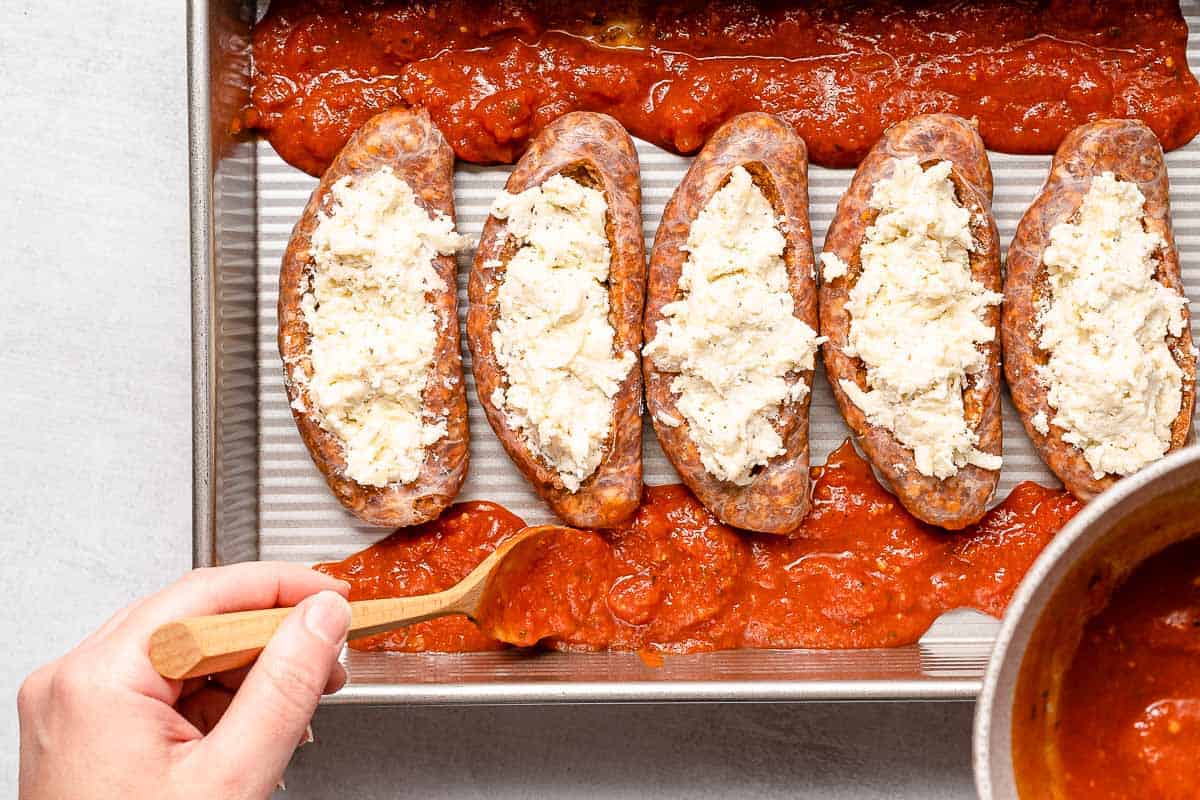 tomato sauce being spooned around stuffed sausages in pan