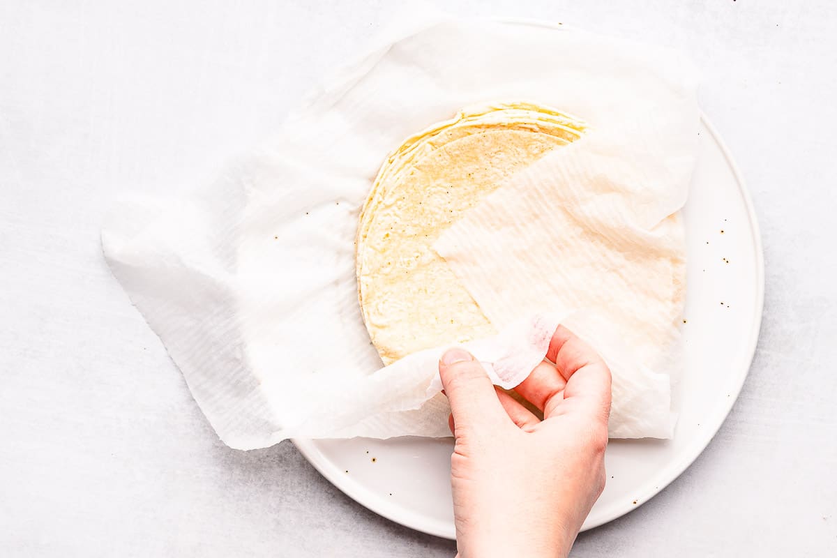hand wrapping damp paper towel around stack of tortillas