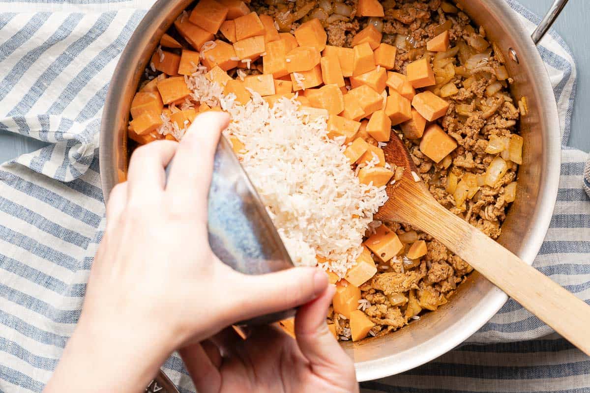 rice being poured into soup pot with sweet potatoes and turkey