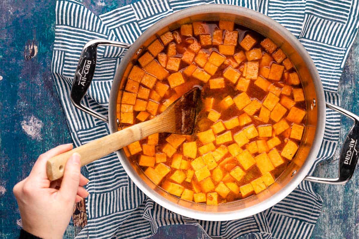 spoon in pot with sweet potato chunks and broth