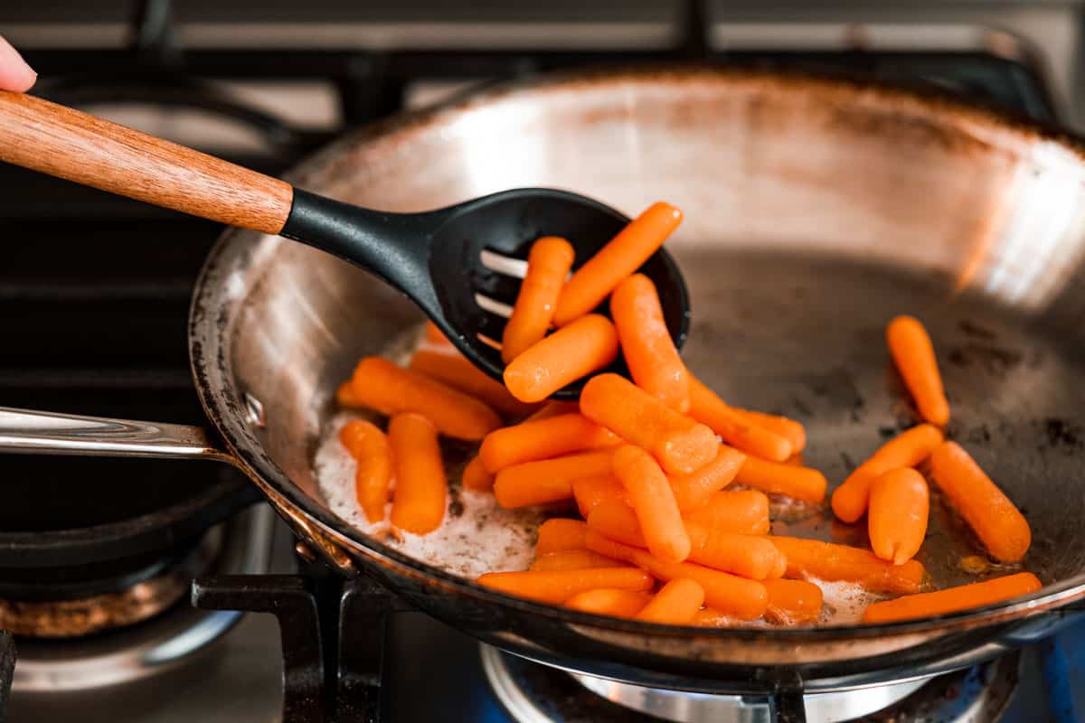 carrots being added to pan on stovetop