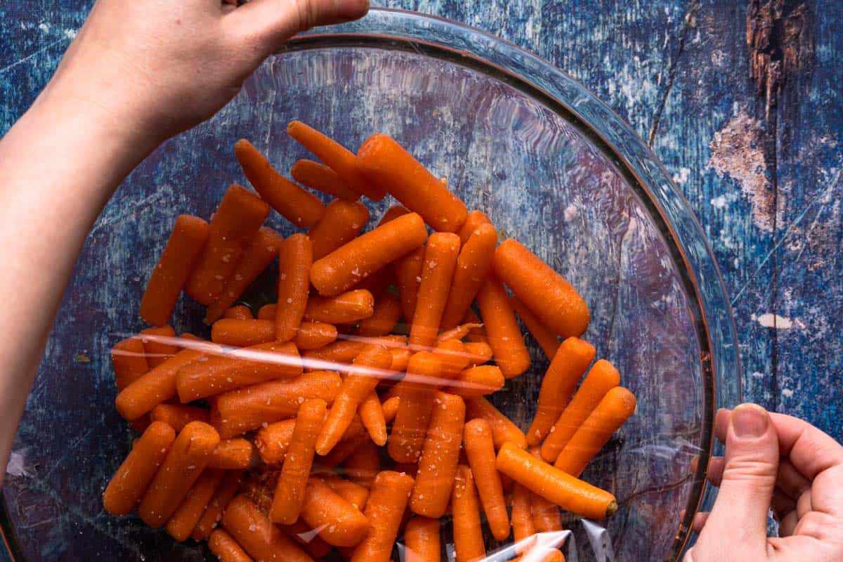 bowl of baby carrots with plastic wrap being applied overtop