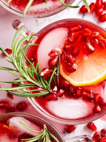 pomegranate cranberry punch in glass garnished with pomegranate seeds and rosemary