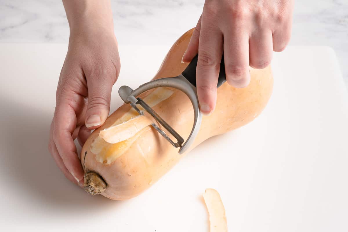 butternut squash being peeled with vegetable peeler