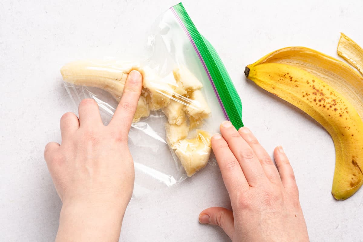 banana inside zip top bag with finger pressing on banana through the bag