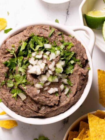 bean dip in bowl with chips and lime on the side