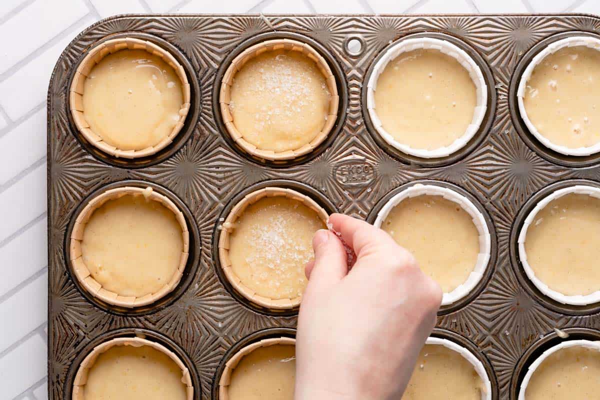 hand sprinkling coarse sugar on top of muffin batter in muffin tin