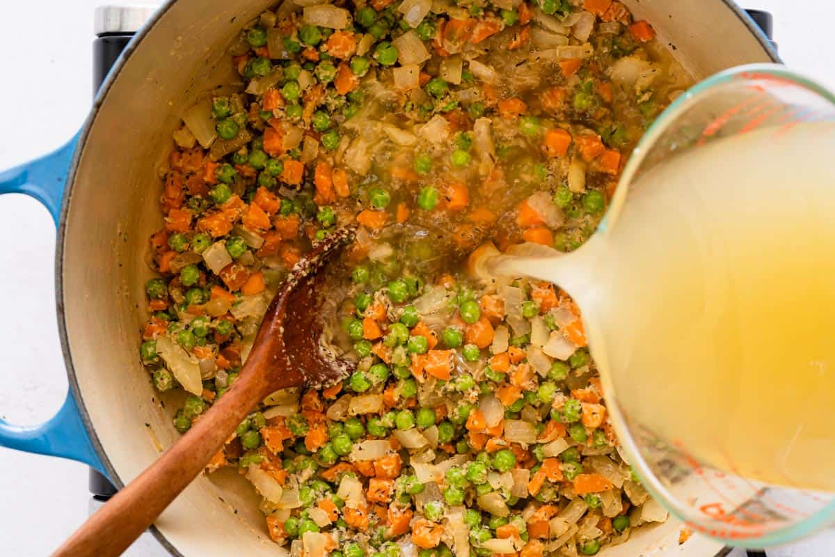 broth being poured into pot with veggies inside