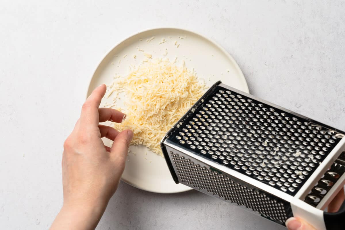 box grater being held overtop plate holding pile of grated Parmesan cheese