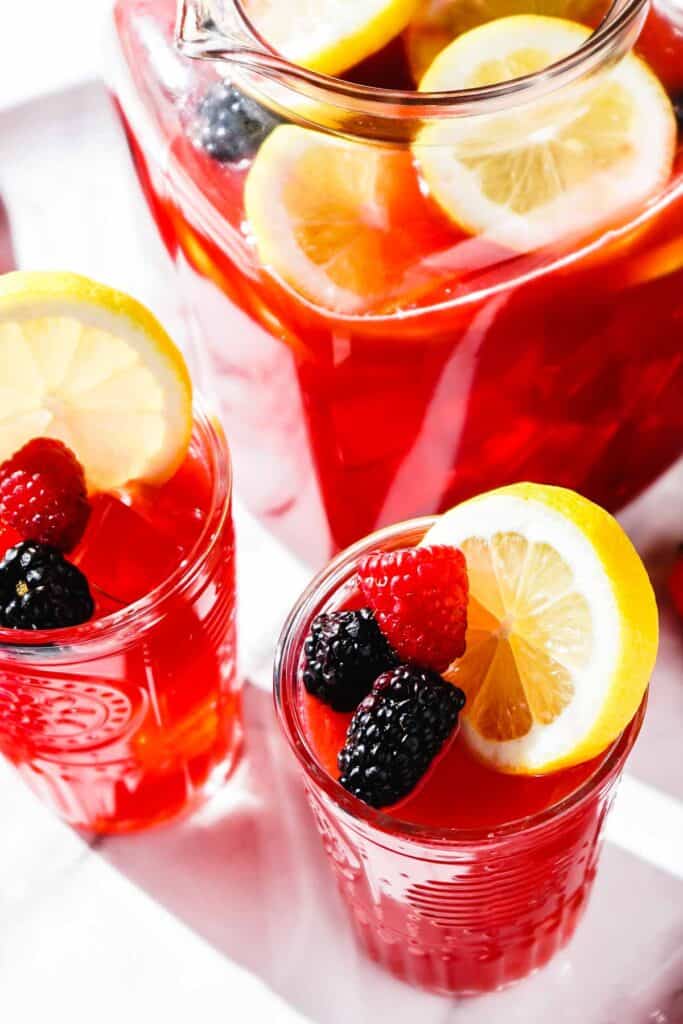 berry lemonade in pitcher and two glasses garnished with berries and lemon slices