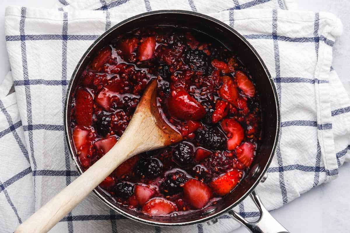 cooked berries and sugar in pot with wooden spoon