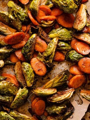 roasted brussels sprouts and sliced carrots on baking pan with spatula on the side