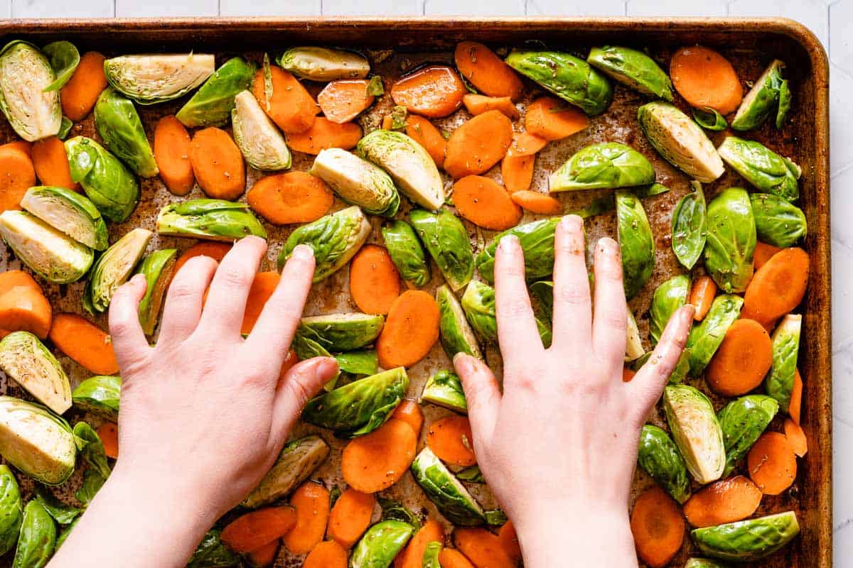 hands spreading out carrots and brussels sprouts on pan