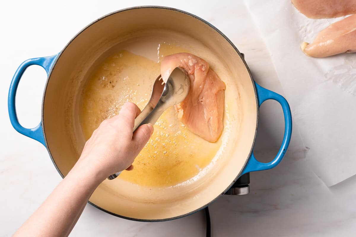 chicken breast being added to Dutch oven with tongs