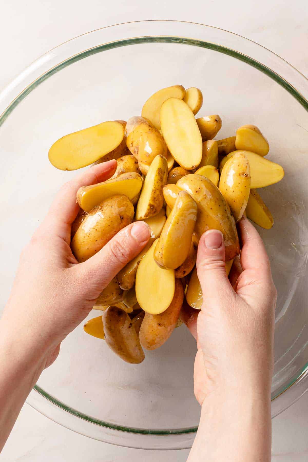 hands tossing cut fingerling potatoes with oil in bowl