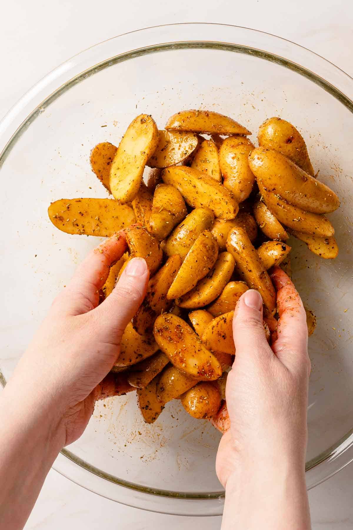 hands tossing potatoes with seasonings in bowl