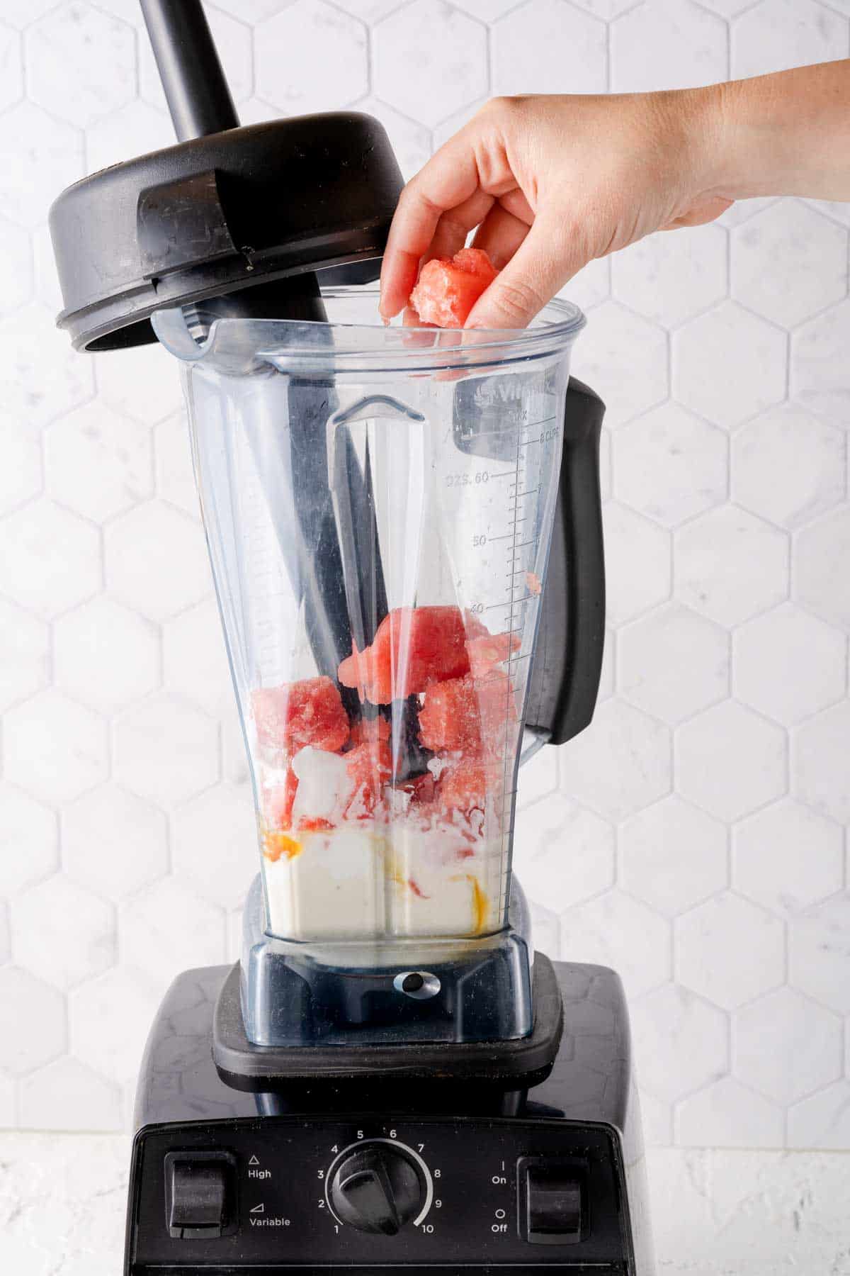 chunks of frozen watermelon being added to blender with other smoothie ingredients inside