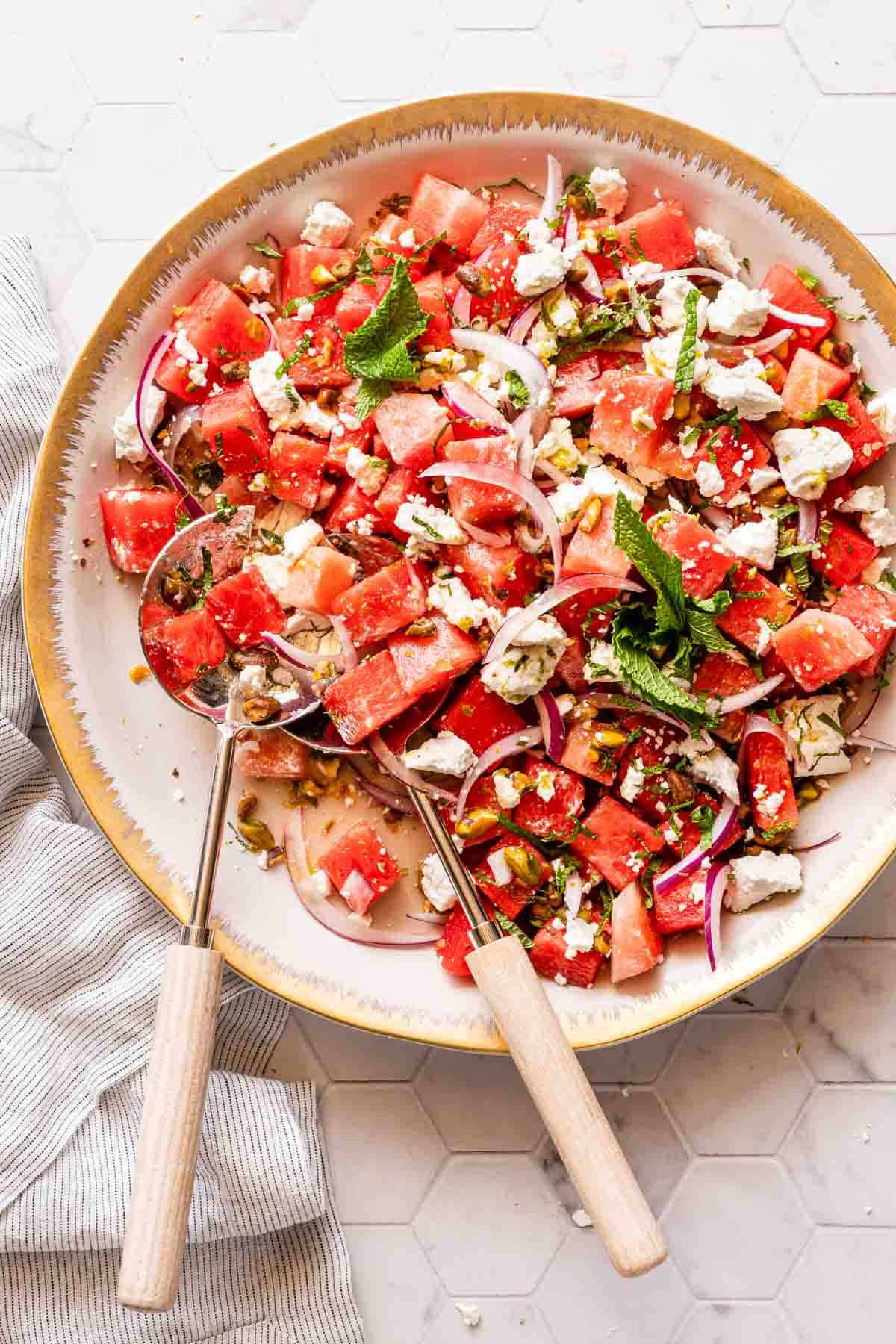 watermelon goat cheese salad on white platter with serving spoons on the side