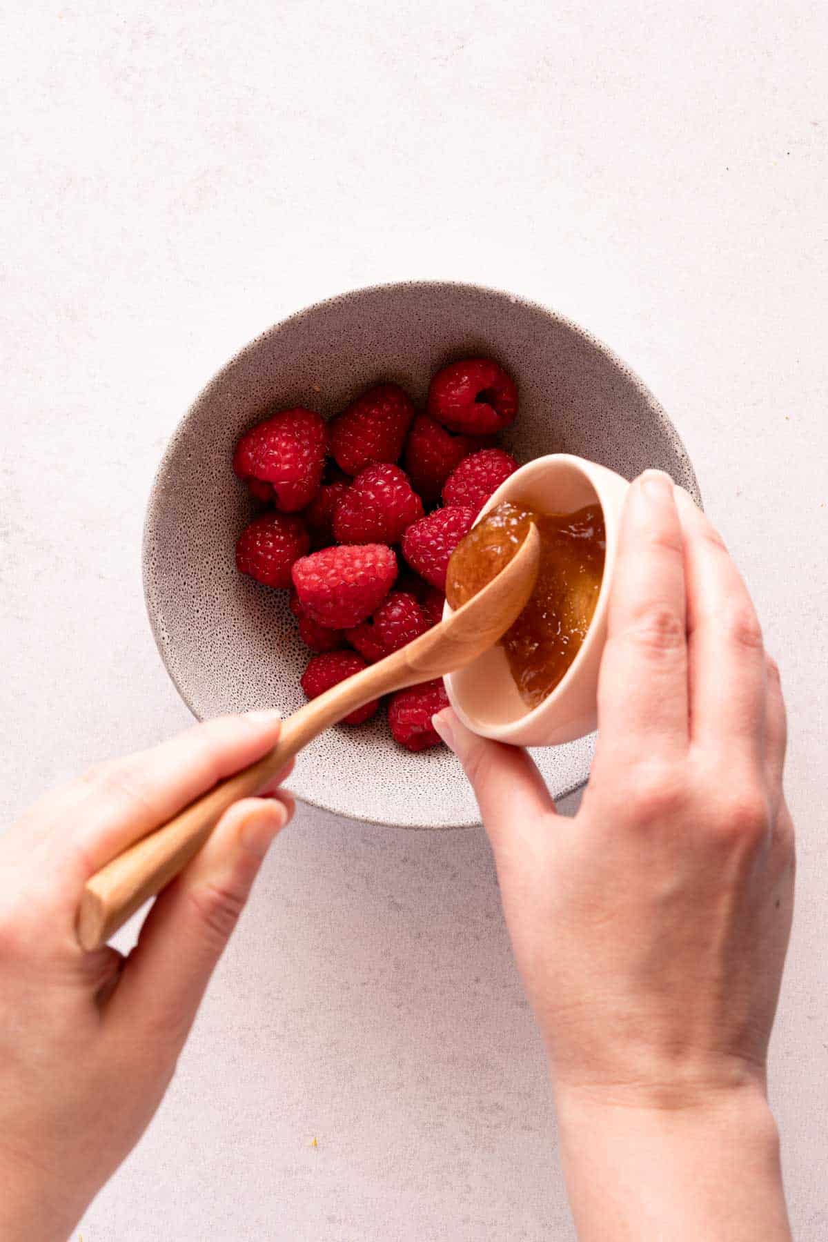 honey being spooned into bowl of raspberries