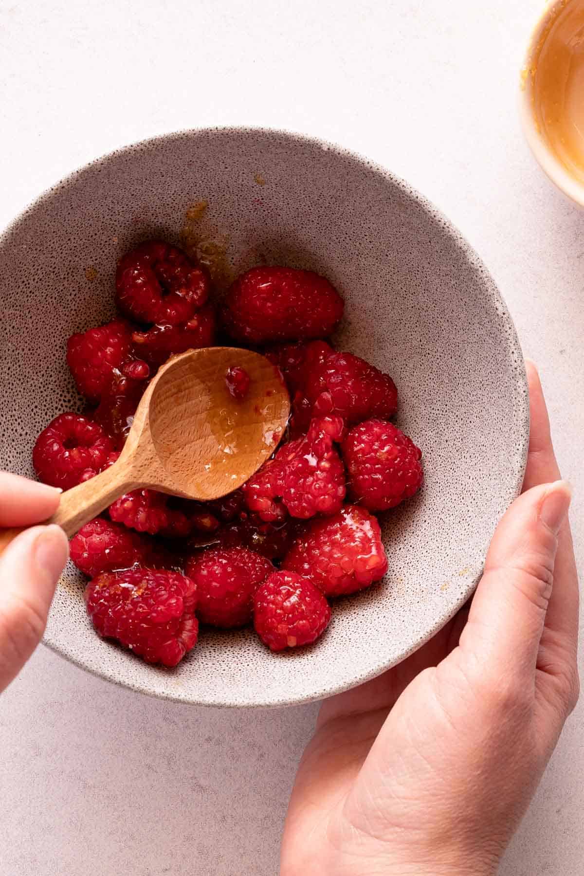 wooden spoon pressing down on raspberries in bowl