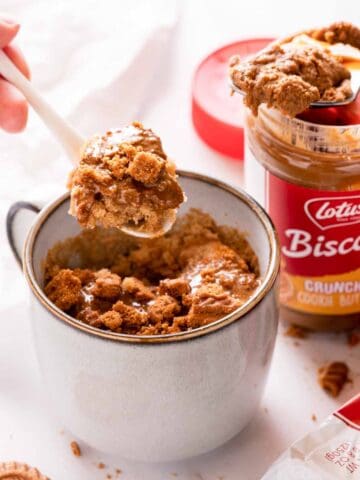 mug cake with Biscoff cookies and Biscoff spread on top and spoon scooping bite out of cake.
