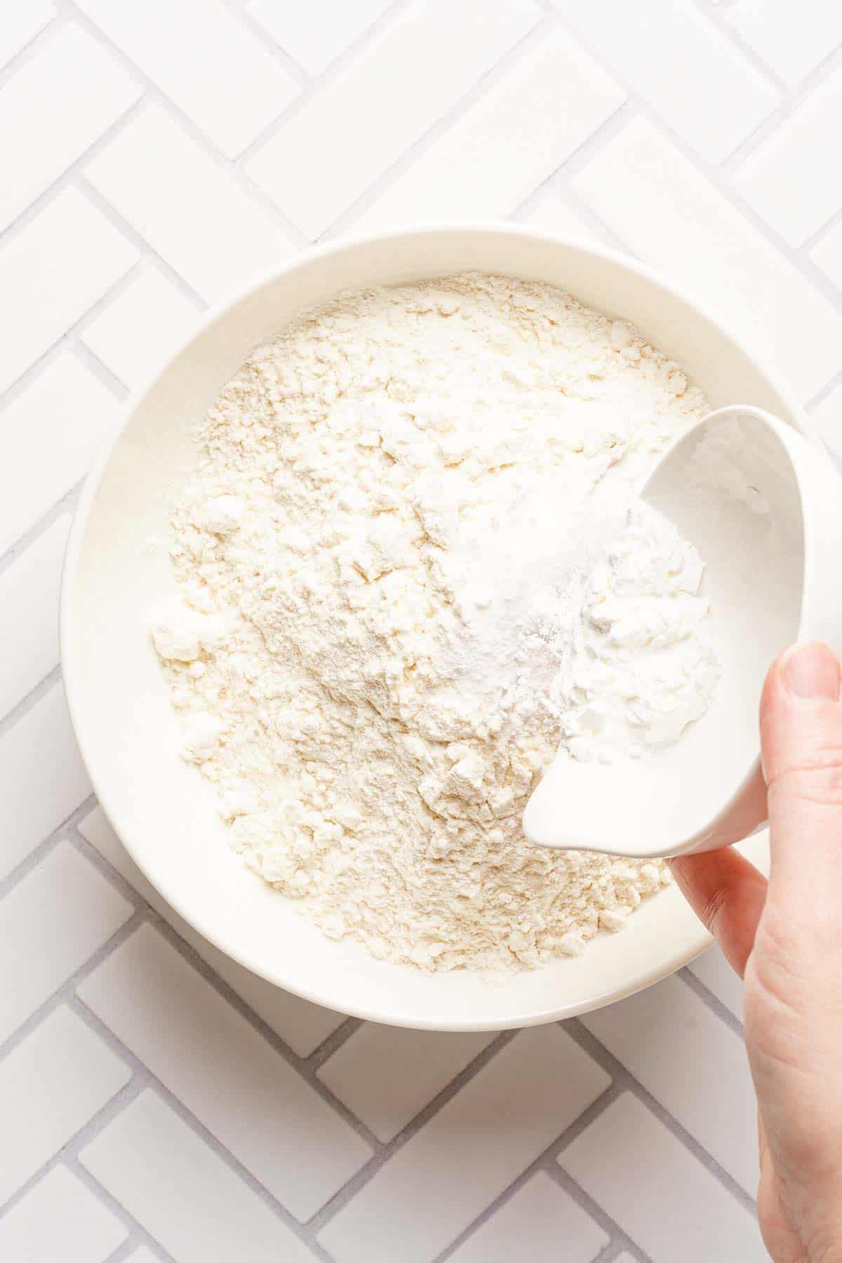 small dish of salt and baking powder being added to a bowl of flour.