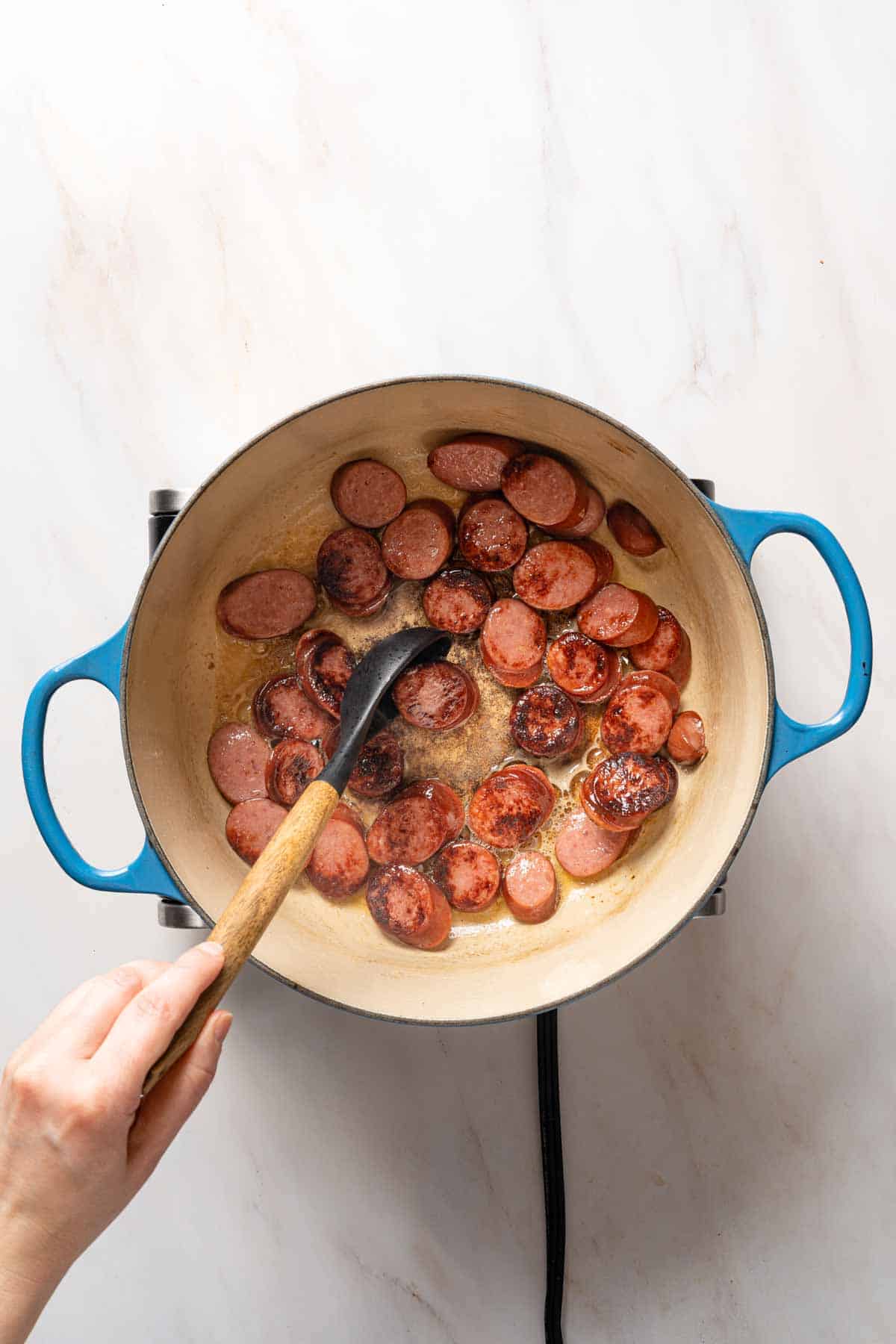 browned kielbasa sausage slices being turned with wooden spoon.