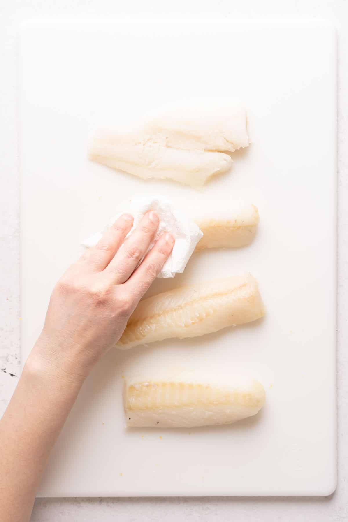 cod pieces being patted with paper towel.