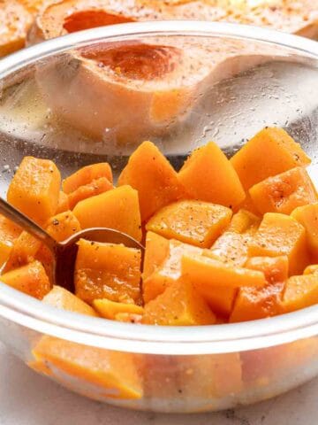 cubes of butternut squash in glass bowl with spoon in bowl.