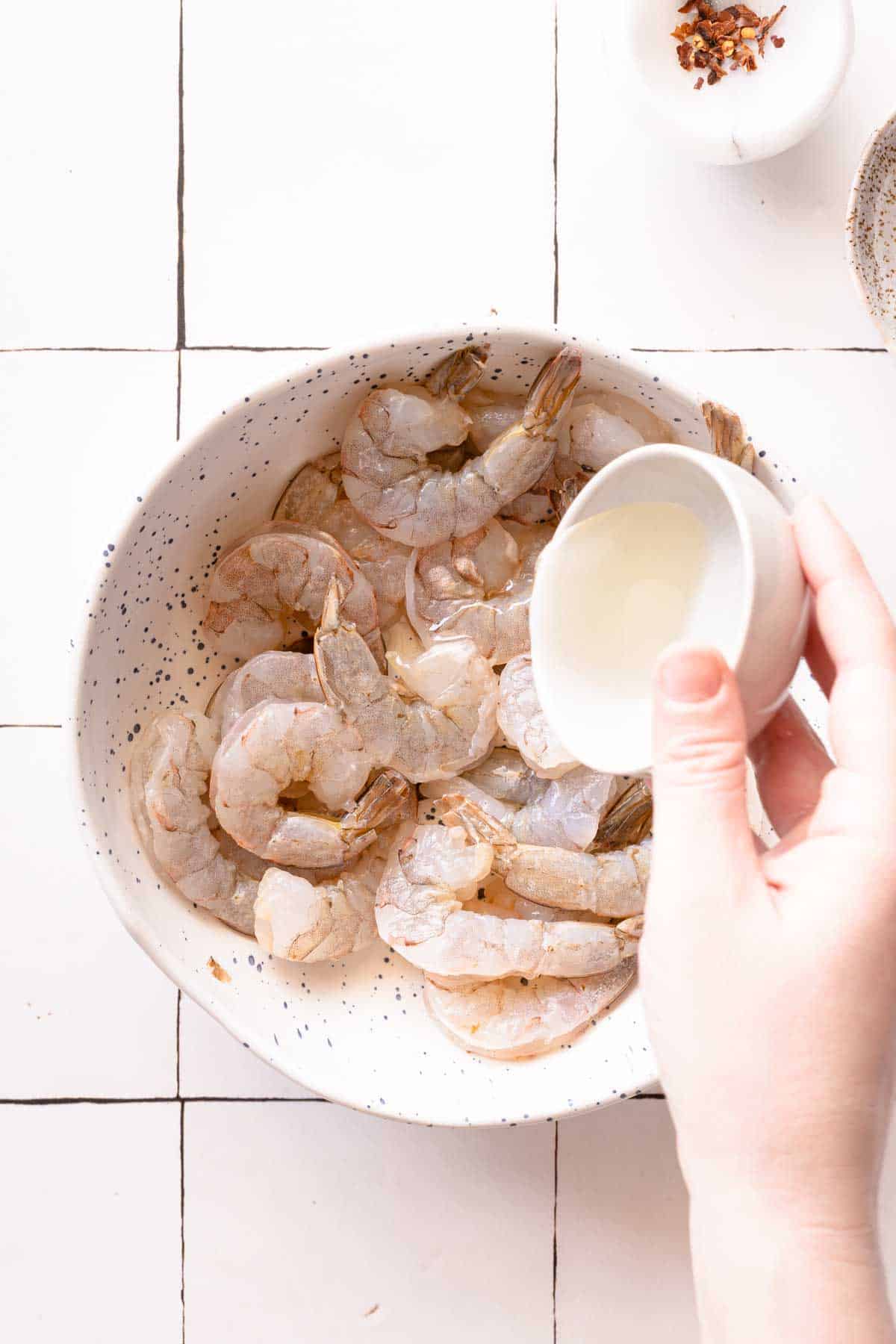 oil being drizzled over raw shrimp in a bowl.