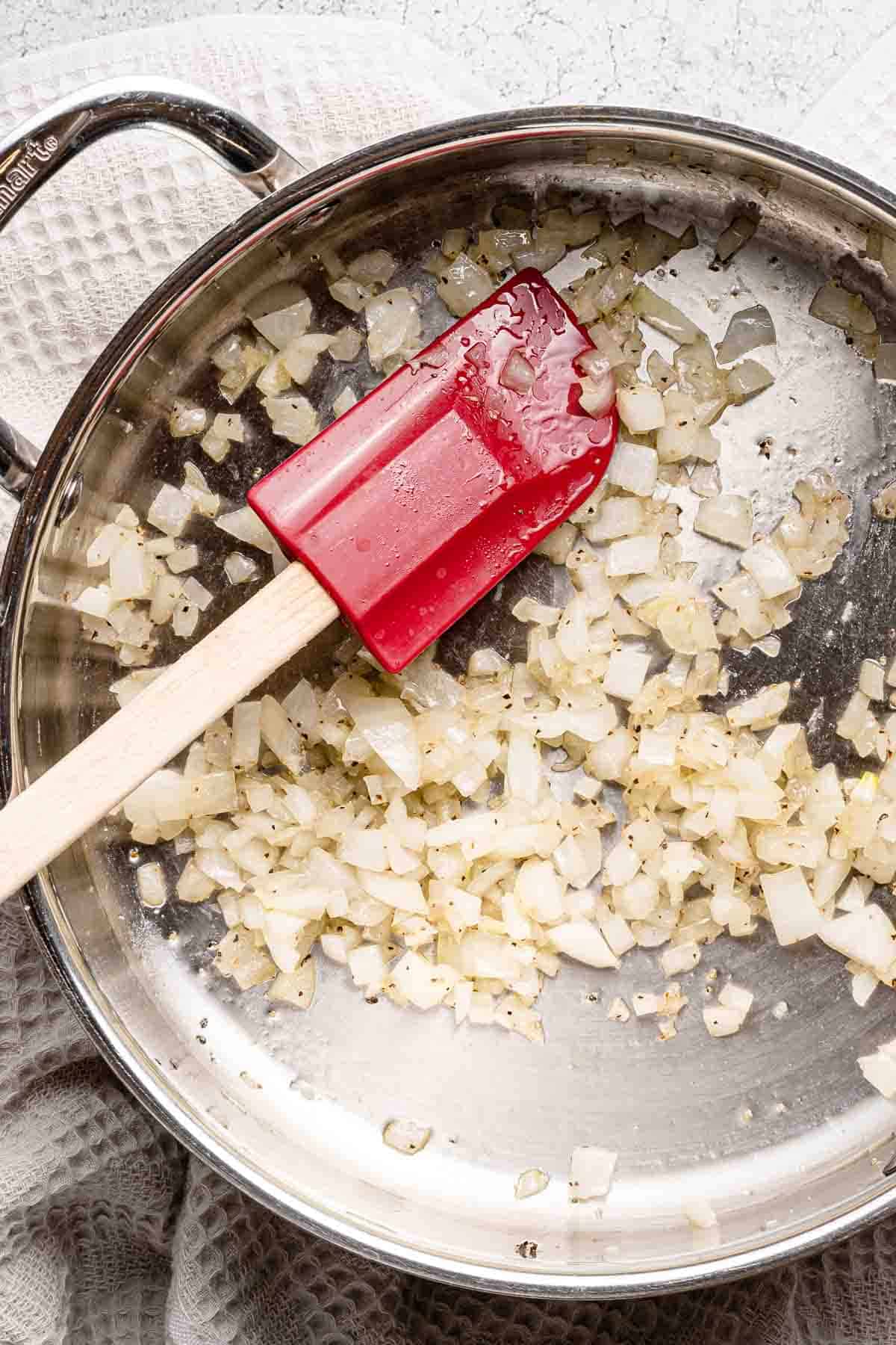 cooked chopped onions in a pan with a rubber spatula.