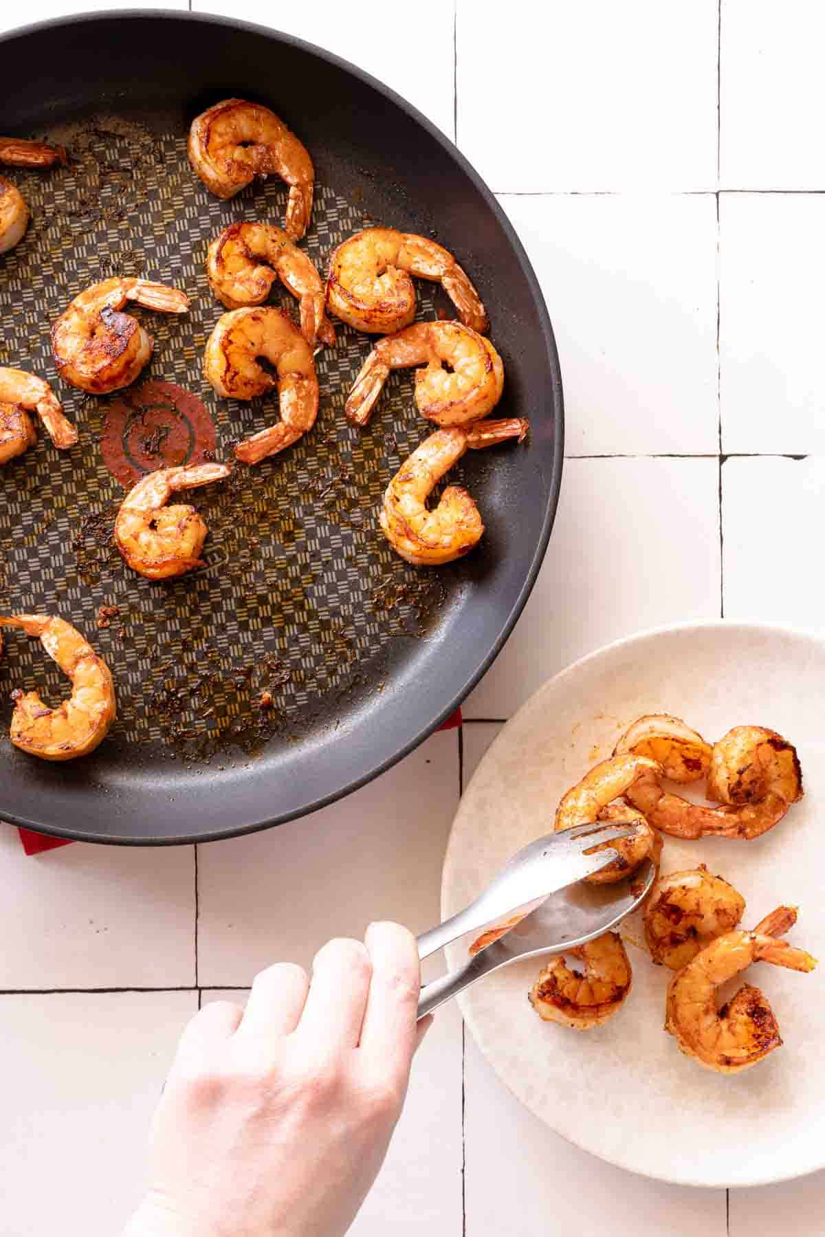 tongs moving shrimp from pan to plate.