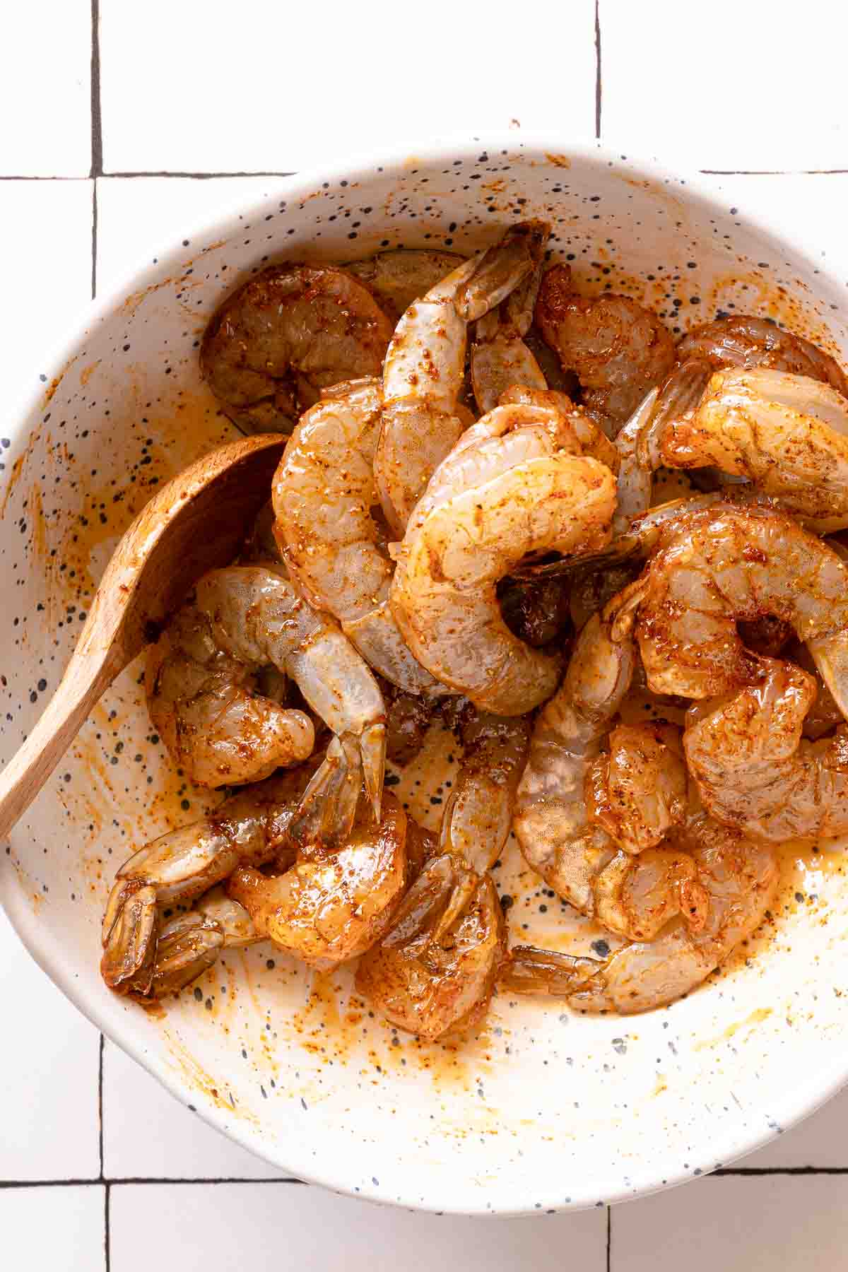 seasoned raw shrimp in bowl with wooden spoon.