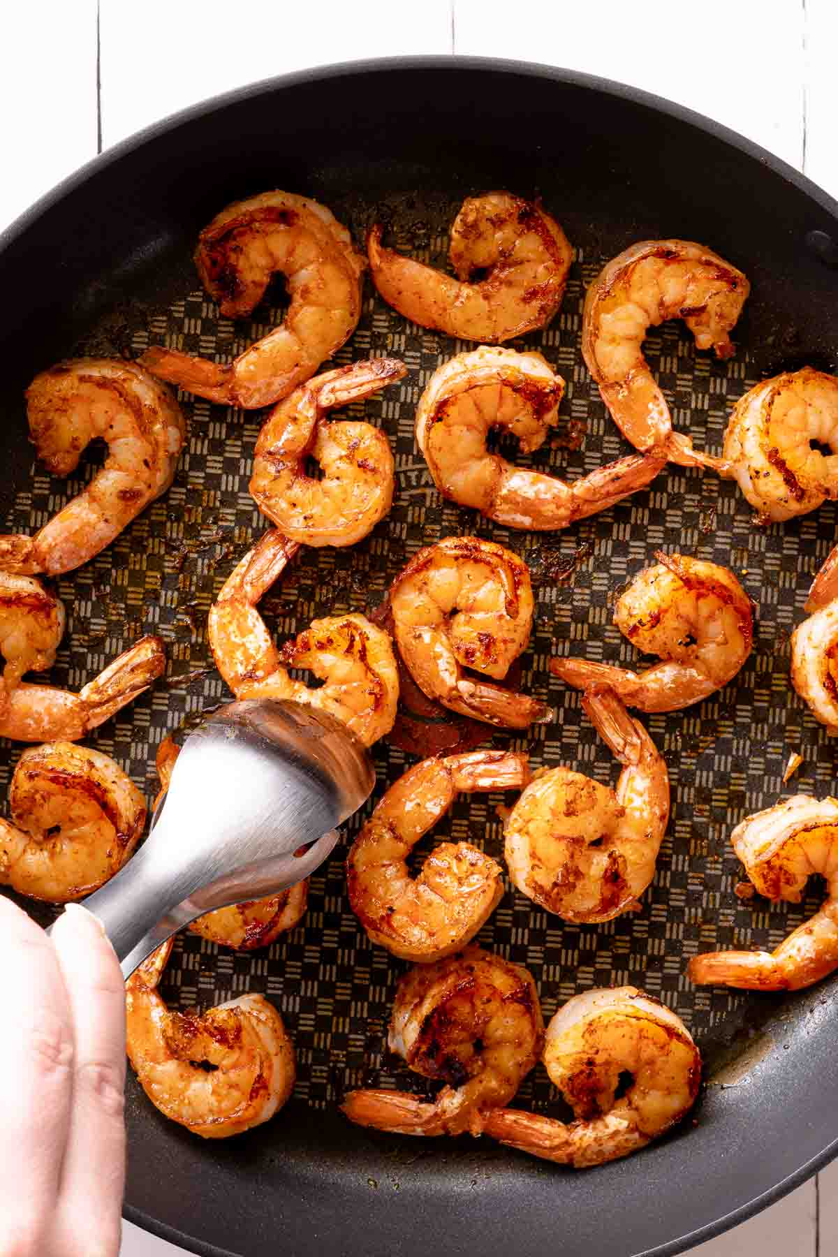 tongs flipping cooked shrimp in pan.