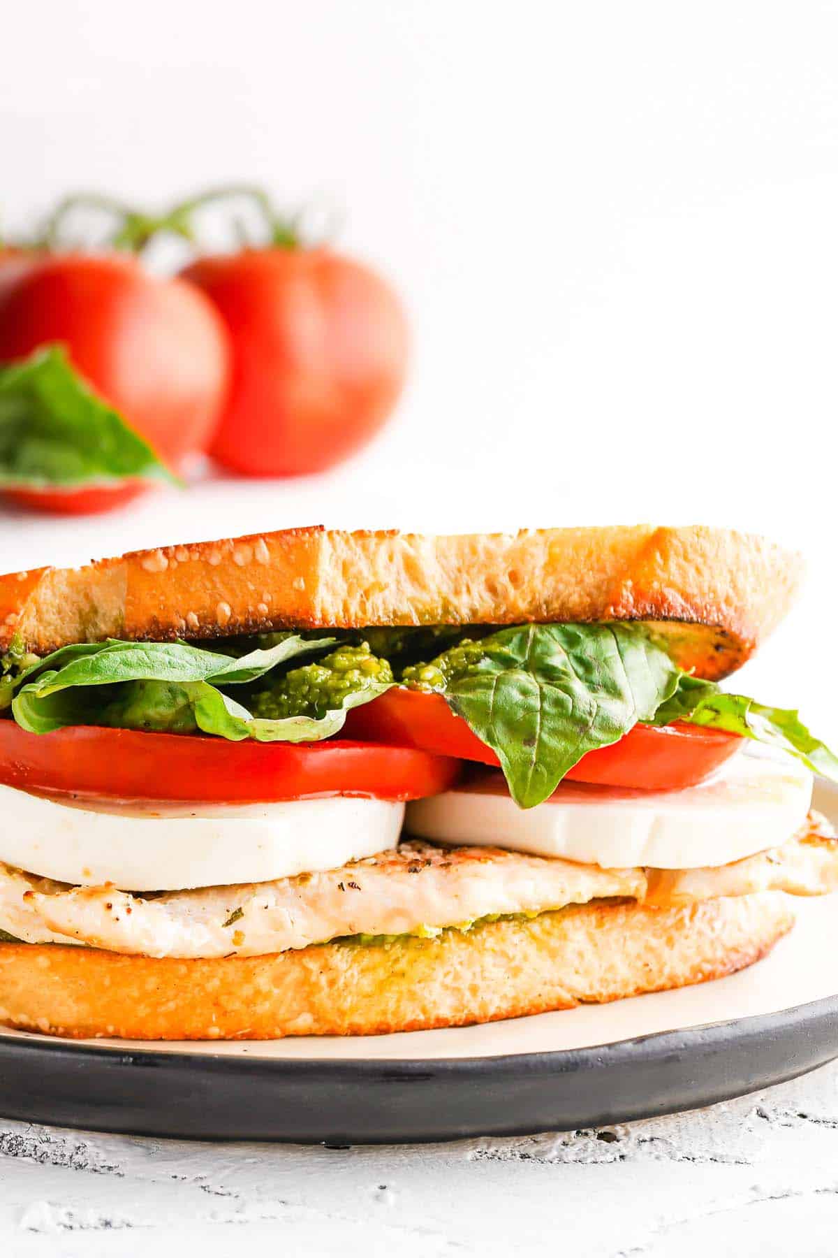 sandwich with chicken tomatoes and basil on plate with tomatoes in the background.