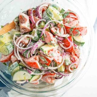 creamy cucumber tomato and onion salad in large glass bowl.