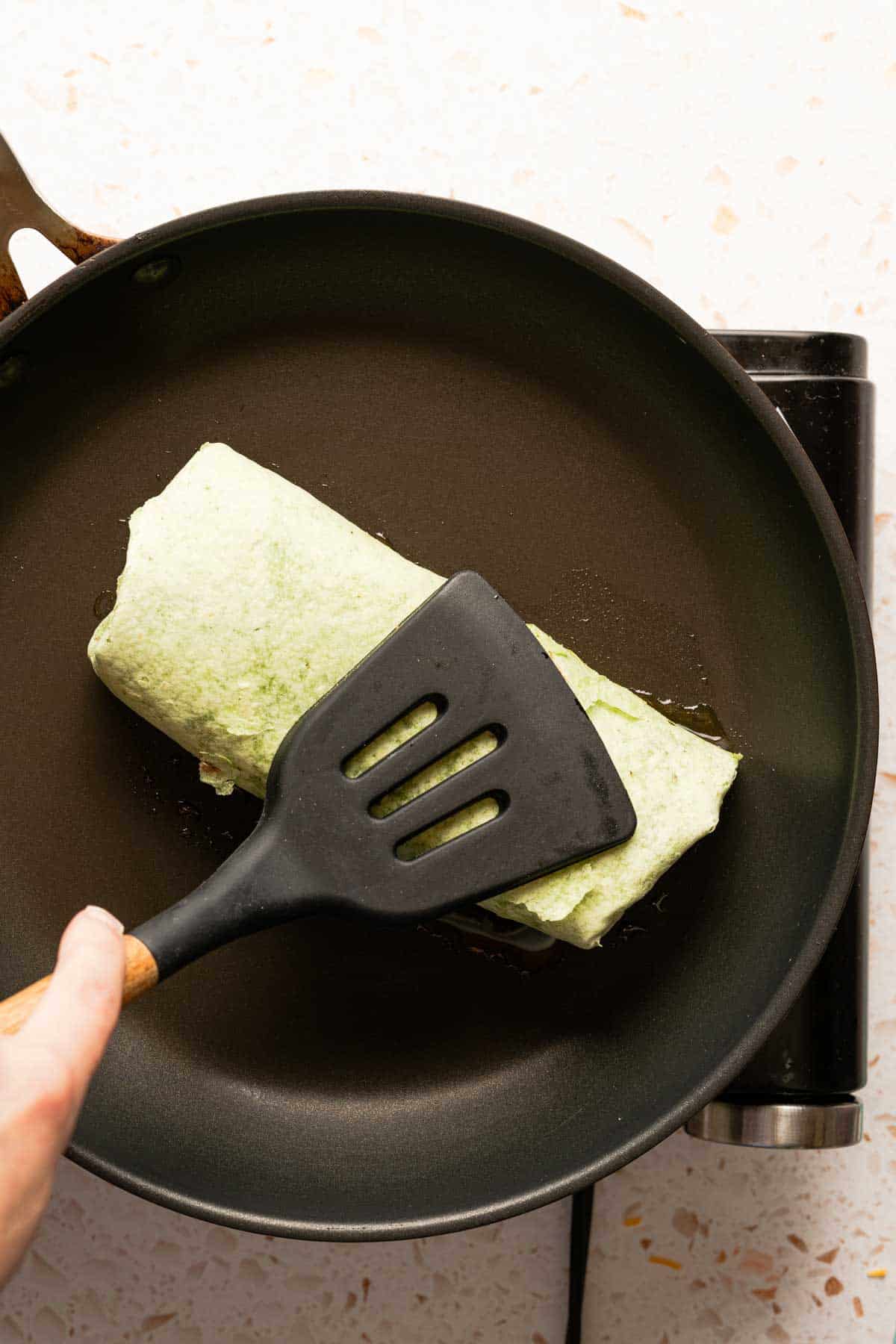 tuna melt wrap being pressed down in pan with spatula.