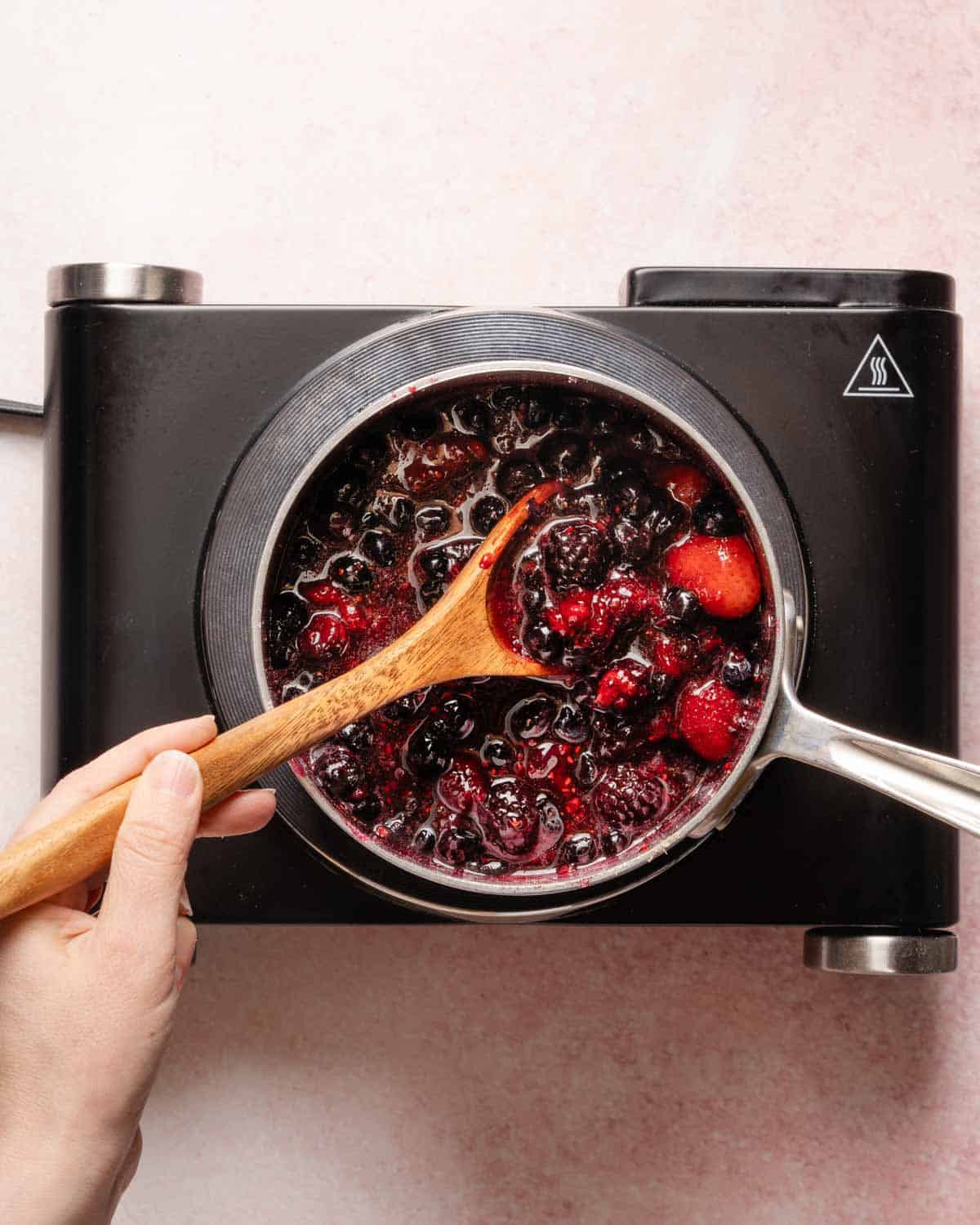 berries and sugar being cooked in small pot on a burner.