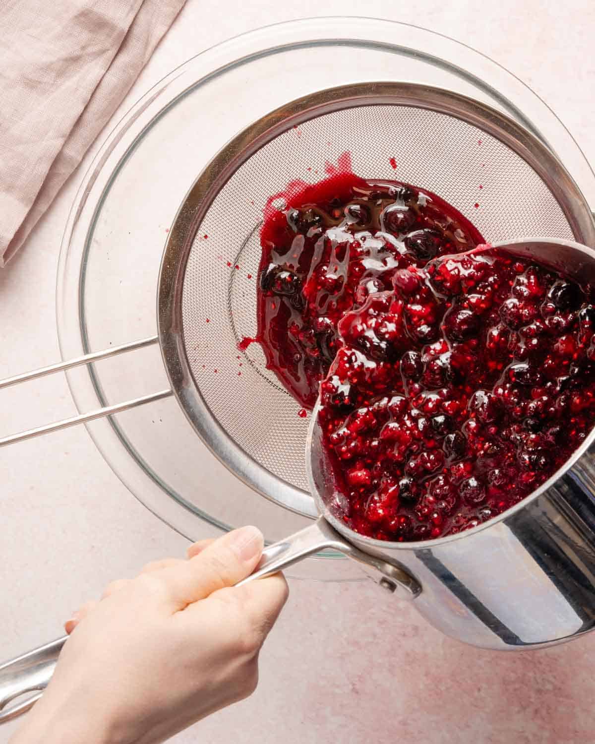 cooked berries being poured into a strainer set over a bowl.