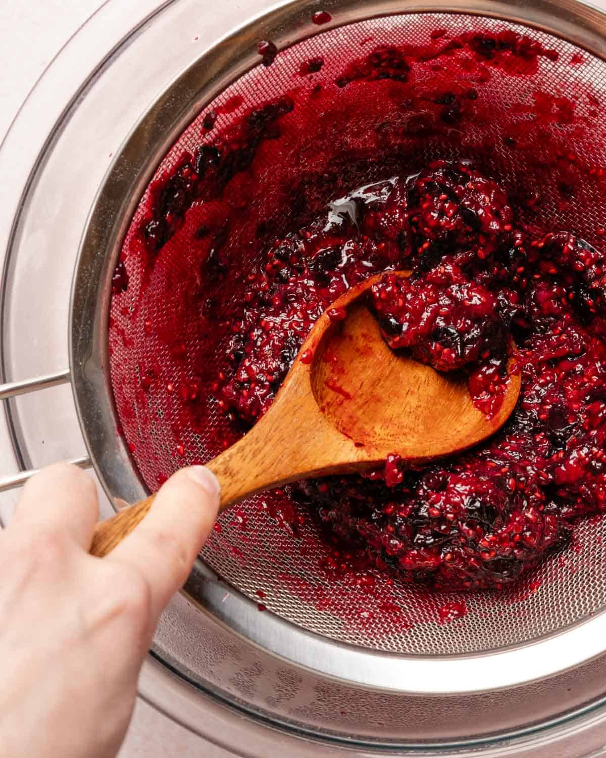 spoon pressing berry pulp through a strainer.