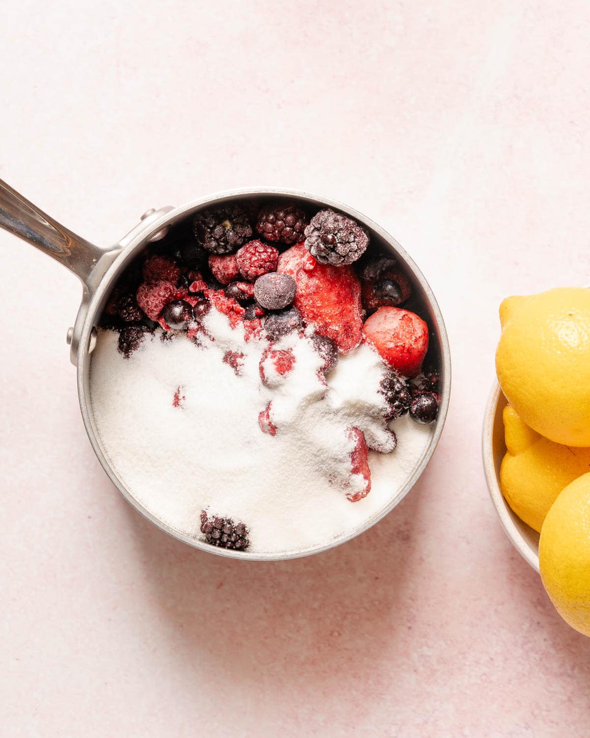 sugar and berries in a pot with lemons on the side.