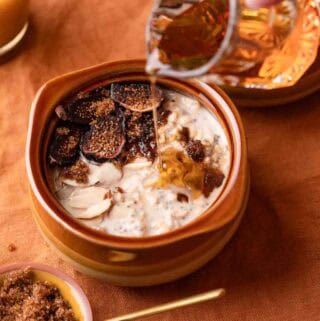 maple syrup being poured over overnight oats topped with fruit and brown sugar.