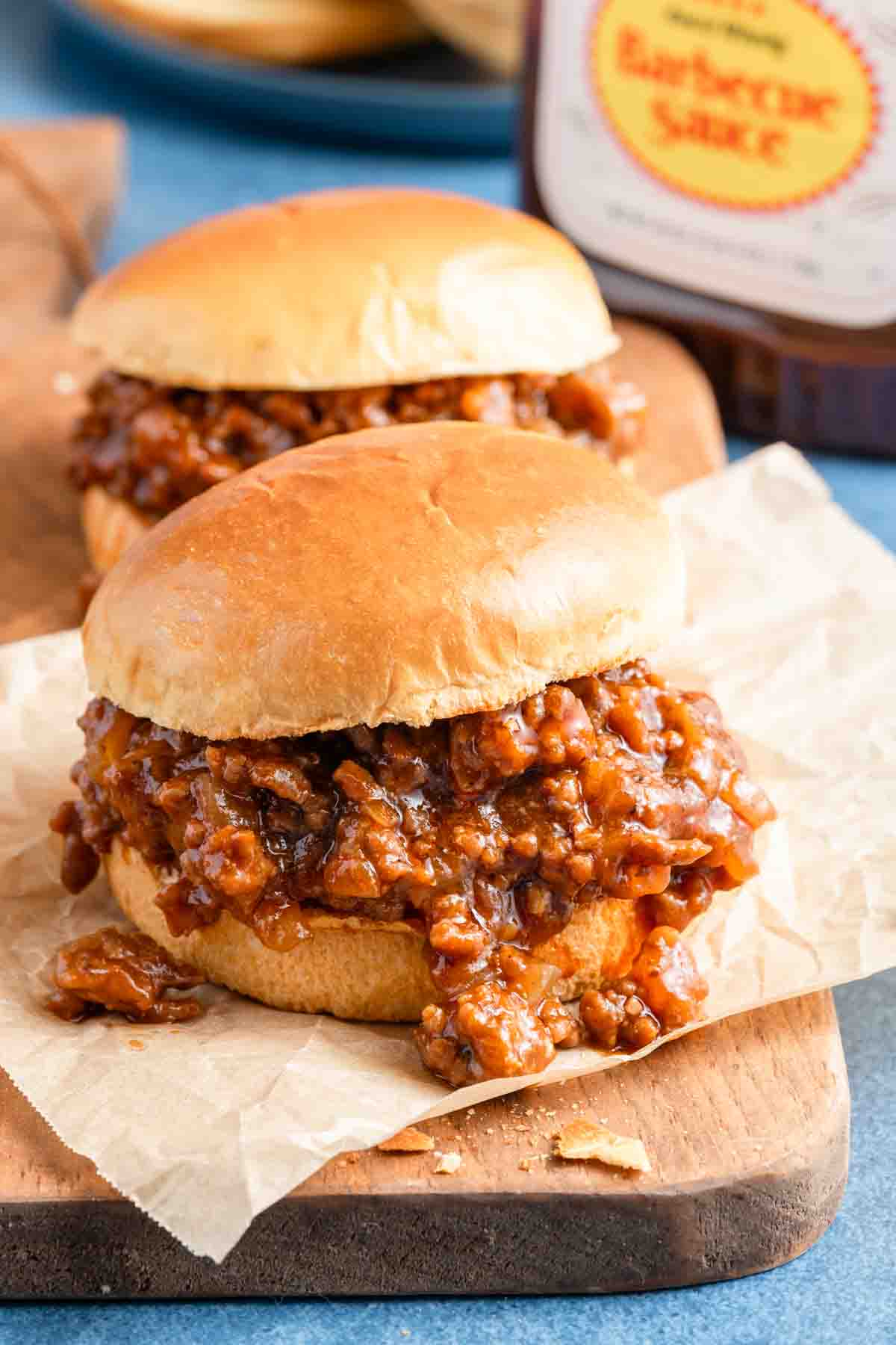 two barbecue sloppy joes on wooden board.