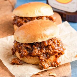 two bbq sloppy joes on board with bbq sauce on the side.