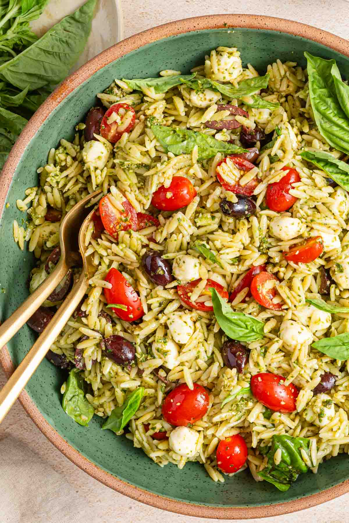green bowl with orzo pesto salad and spoons for serving.
