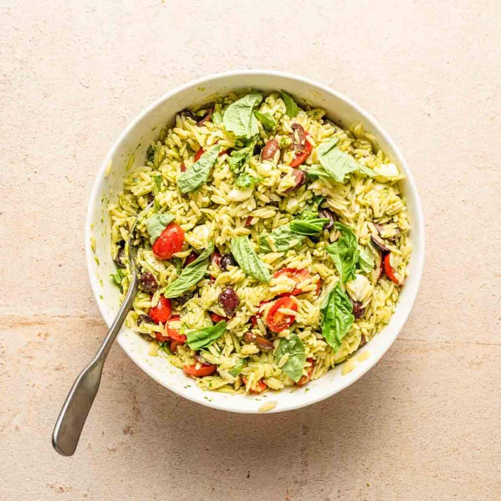 orzo pesto pasta salad in white bowl garnished with fresh basil leaves.