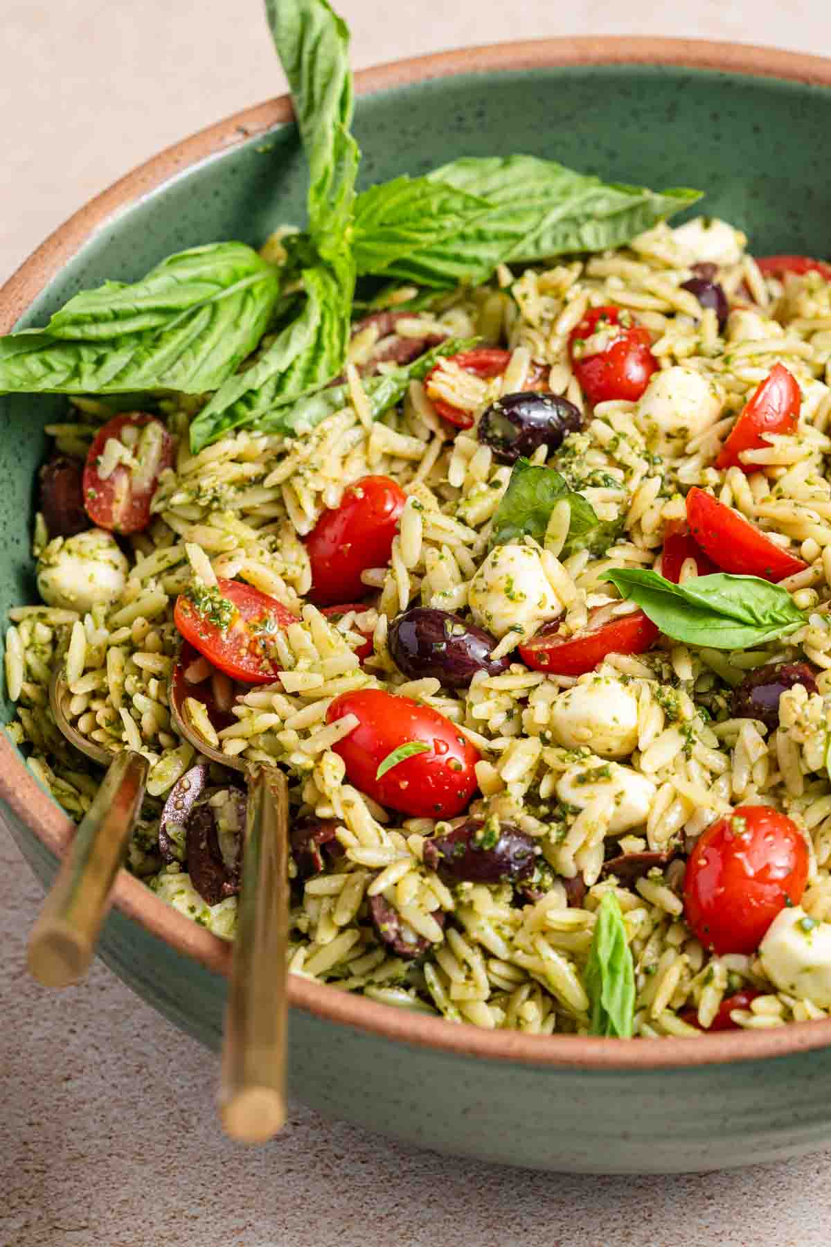 green bowl of orzo salad garnished with basil leaves.